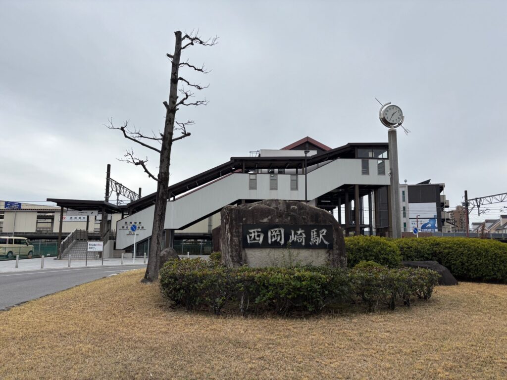 JR西岡崎駅 北口｜「西岡崎駅」と刻まれた自然石の駅名標・高架駅舎・丸型時計ポール 岡崎矢作南はなえみ墓園へ車で6分