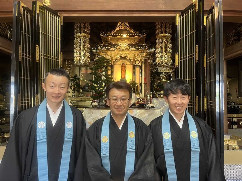 正法寺 住職・長谷部俊成師（中央）と若い僧侶2人（左右）が金色の本堂内陣（阿弥陀如来・宮殿）を背に並ぶ