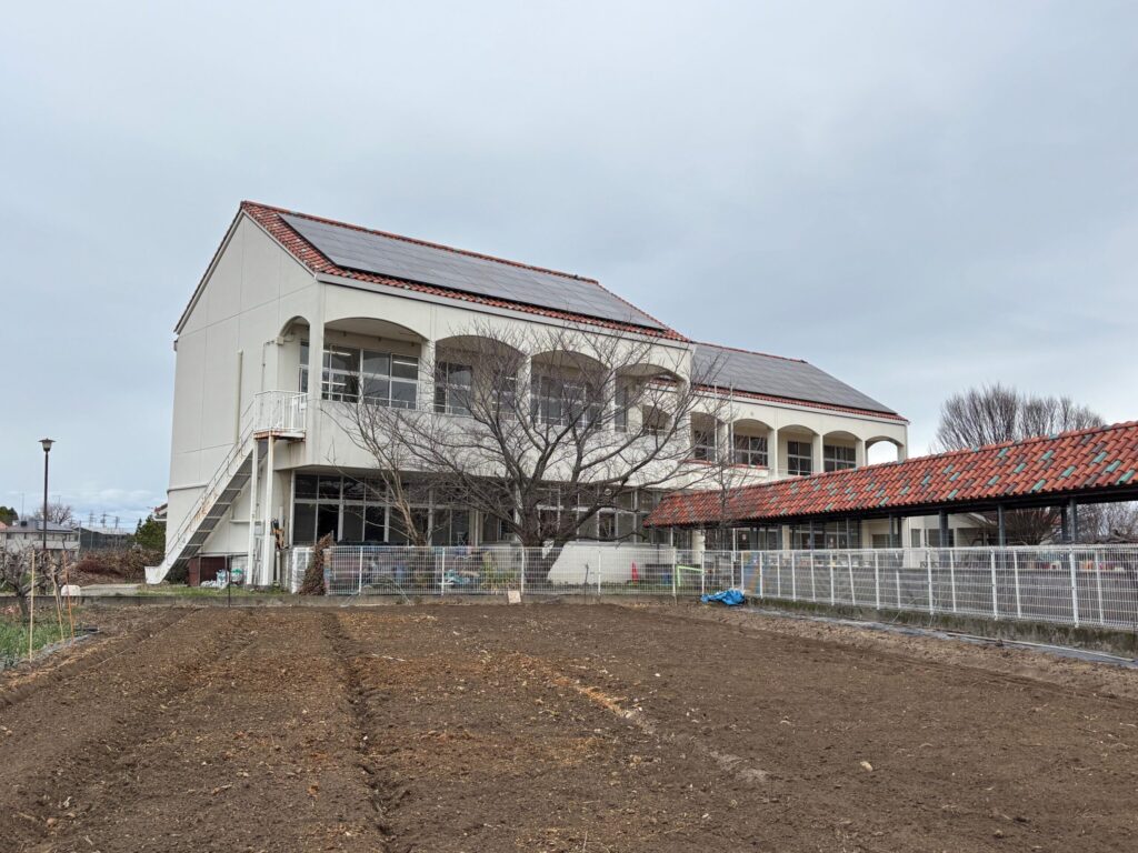 矢作みやこ幼稚園（岡崎市東本郷町周辺）｜白い2階建て校舎・テラコッタ屋根・太陽光パネル・前景に農地 岡崎矢作南はなえみ墓園周辺のランドマーク