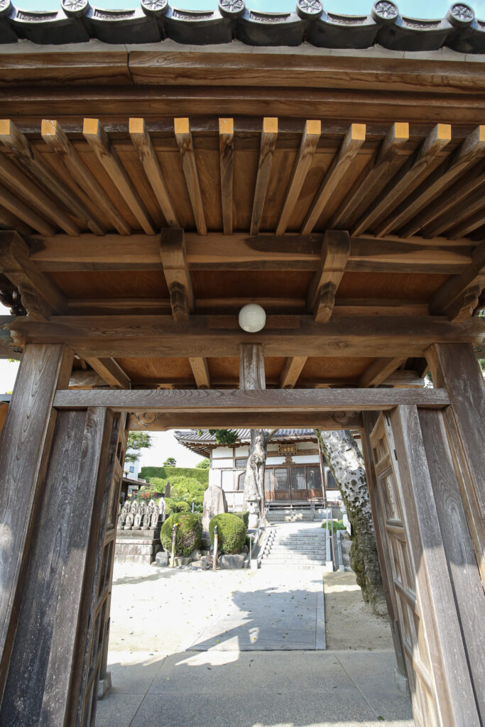 曹洞宗 嶺松山 本覚寺の山門越しに望む本堂｜整えられた境内と石仏群（知多市八幡）