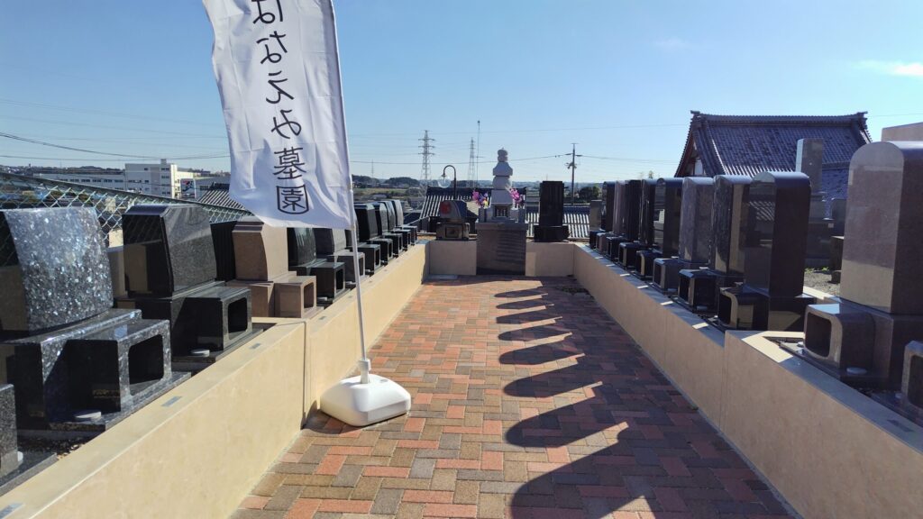 豊橋高師はなえみ墓園のシンボル｜白御影石の五輪塔・色とりどりの献花・両脇に和型墓石・背景に紫雲寺本堂の瓦屋根