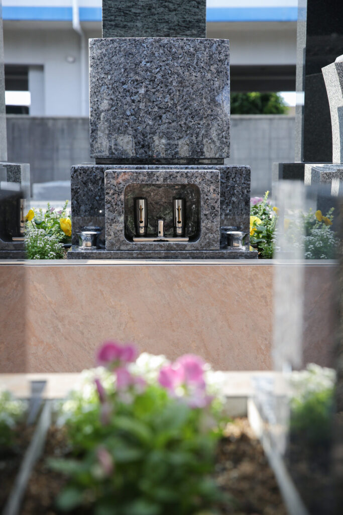 常滑はなえみ墓園のメインビジュアルです。1322年（鎌倉時代末期）創建、703年の法灯を護り続ける臨済宗妙心寺派・海音寺（かいおんじ）の本堂を背景に、はなえみ墓園のお墓が整然と並びます。中央右の白いのぼり旗が「はなえみ墓園」の目印。寺院本堂・檀信徒墓・はなえみ墓園区画が一体化した寺院墓地ならではの動線で、納骨式・年忌法要直後にすぐお墓へお参りできる利便性があります。住職は磯谷興村（いそがいこうそん）上人。お墓の継承者がいなくても、海音寺が永代にわたりご供養を続けます。和型99万・洋型89万・板型69万円（税込／永代使用料・墓石・文字彫刻・工事費・永代供養料すべて込み）。