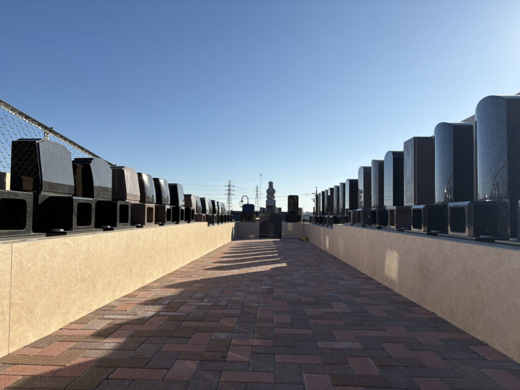 豊橋高師はなえみ墓園 参道全景｜赤レンガ敷きの参道・両側に整然と並ぶ磨かれた洋型墓石・遠景に五輪塔・澄み切った青空と地平線