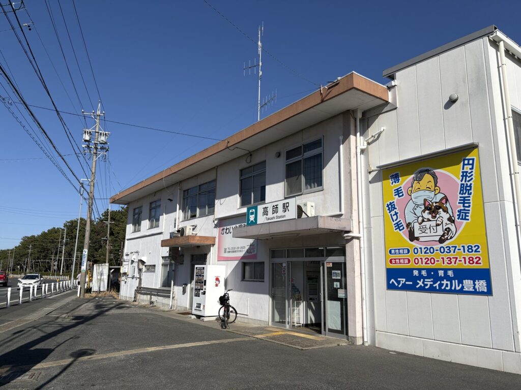 豊橋鉄道渥美線「高師駅」外観｜白い2階建て駅舎・自転車駐輪・松林の遠景（旧高師原）｜豊橋市西高師町