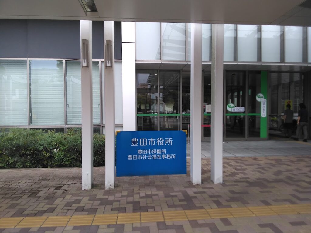 豊田市役所 玄関エントランス｜「豊田市役所・豊田市保健所・豊田市社会福祉事務所」の青い案内板 豊田はなえみ墓園から車で約15分