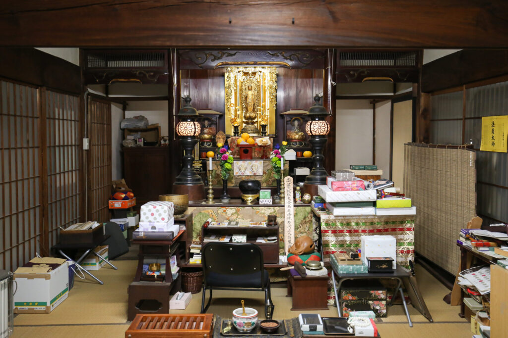 専修院 本堂内陣全景 須弥壇 阿弥陀如来立像 金色装飾 黒漆塗り灯籠 「浄財」と書かれた賽銭箱 茶色畳 「法雨大師」の黄色札 整然と並ぶ供物