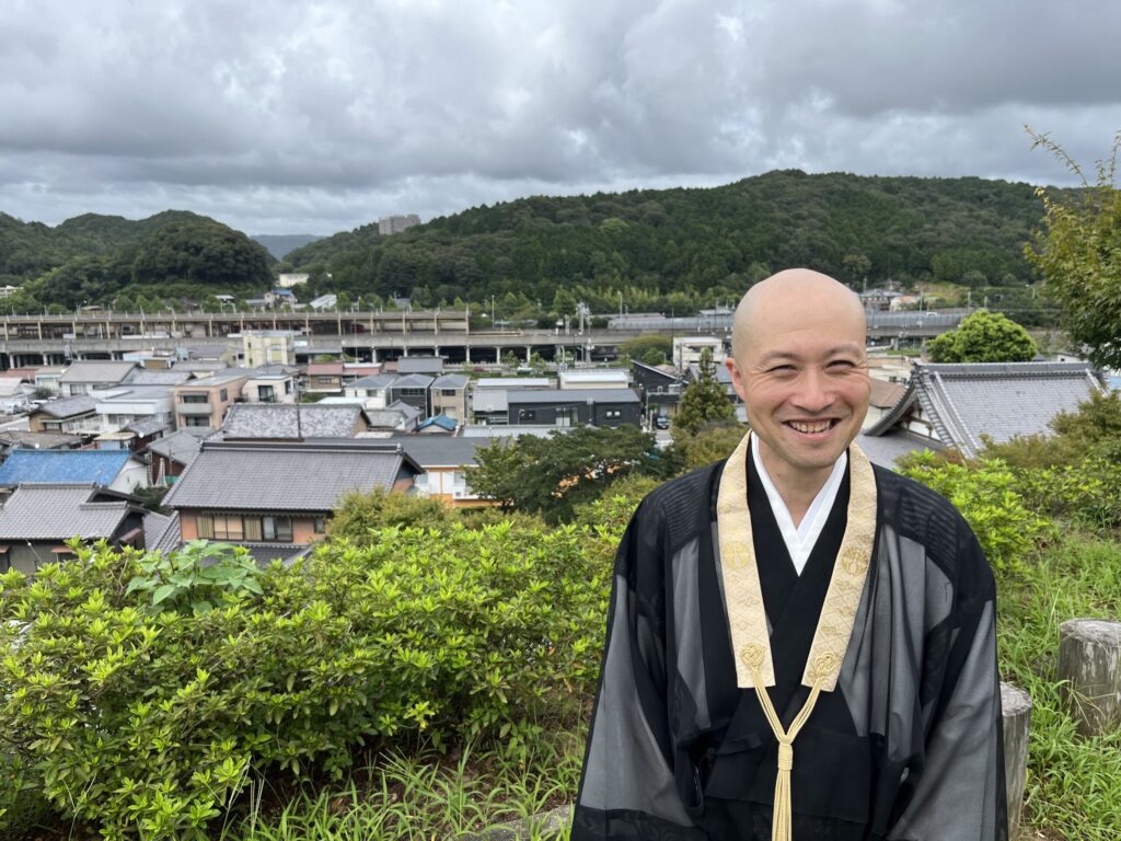 桜山を背に本宿の町並みを見下ろし笑顔で立つ欣浄寺住職