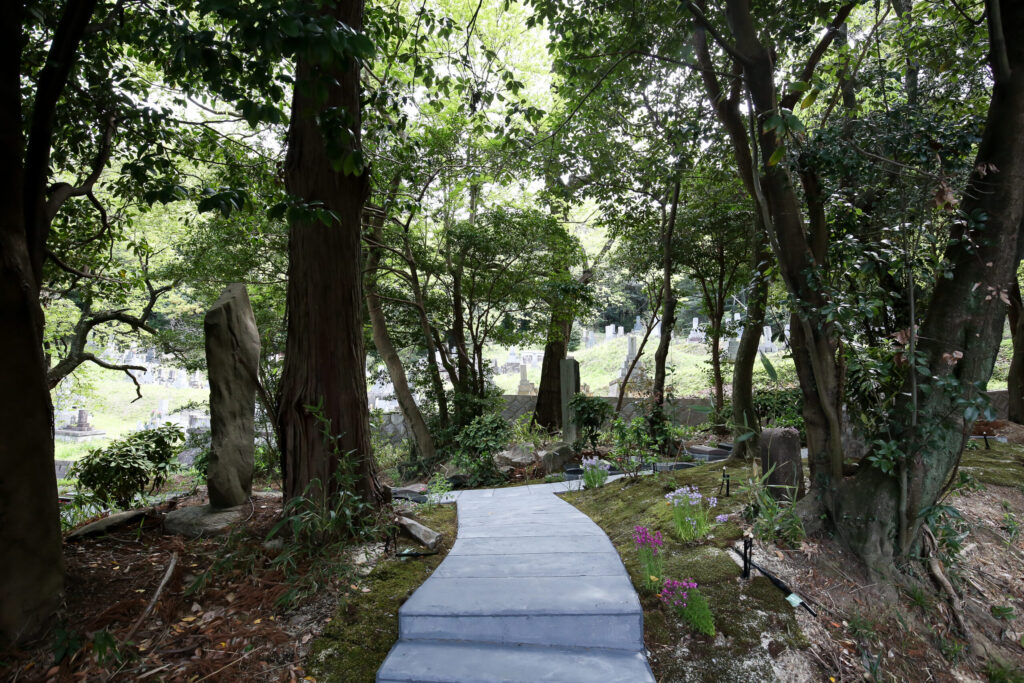 木立の中の石段の先に在来墓地を望む樹木葬区画（阿久比はなえみ墓園・谷性寺）