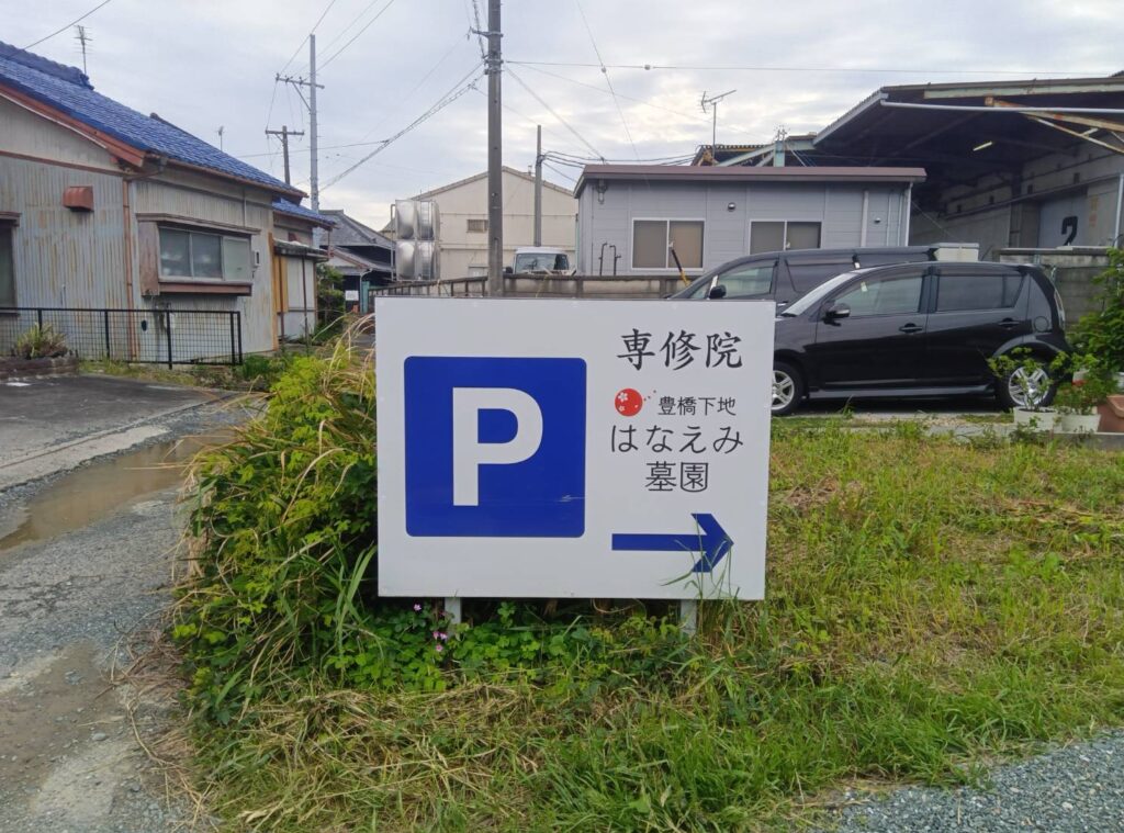豊橋下地はなえみ墓園 専修院 駐車場案内看板 青地白Pマーク 「専修院 豊橋下地はなえみ墓園」「→」赤梅花マーク 周辺の住宅街