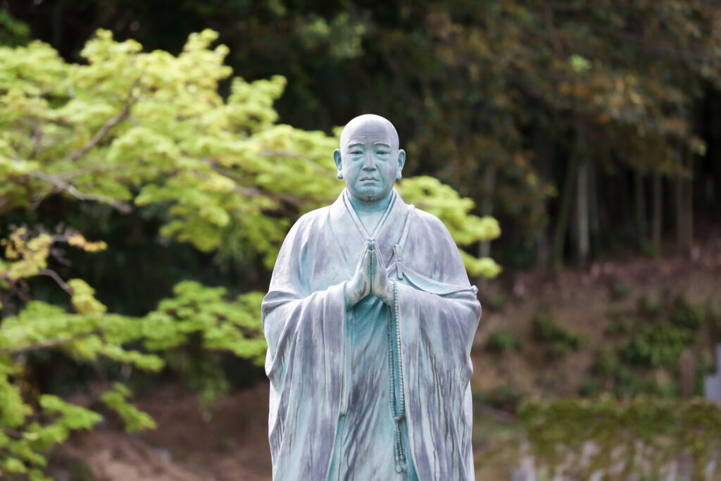 新緑を背に合掌する僧侶の銅像（谷性寺）