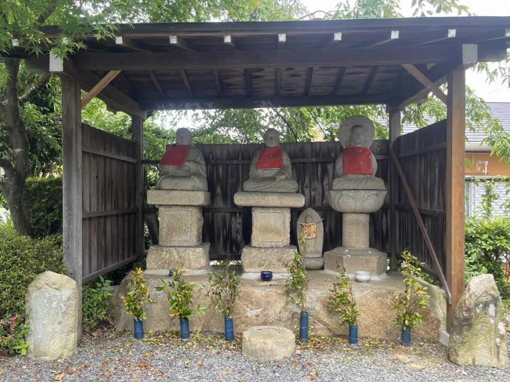 赤い前掛けを掛けられ屋根の下に並ぶ欣浄寺境内の石仏三尊