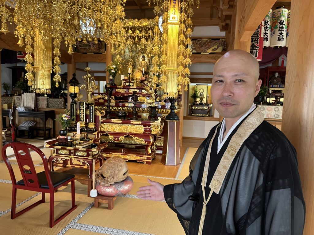 金色の天蓋が連なる欣浄寺の内陣で参拝者を手で迎える住職